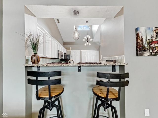 kitchen featuring stainless steel microwave, a peninsula, white cabinetry, and lofted ceiling