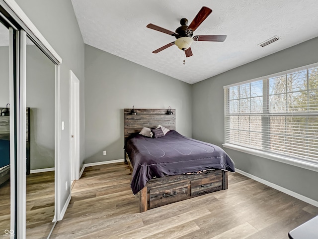 bedroom featuring visible vents, lofted ceiling, wood finished floors, a closet, and a textured ceiling