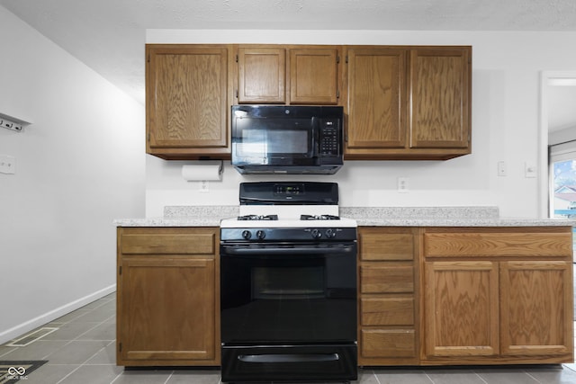 kitchen with brown cabinets, light tile patterned floors, light countertops, black appliances, and baseboards