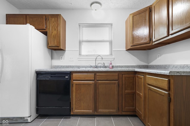 kitchen featuring black dishwasher, light tile patterned floors, brown cabinetry, freestanding refrigerator, and a sink