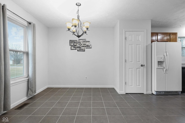 unfurnished dining area featuring dark tile patterned floors, an inviting chandelier, visible vents, and baseboards