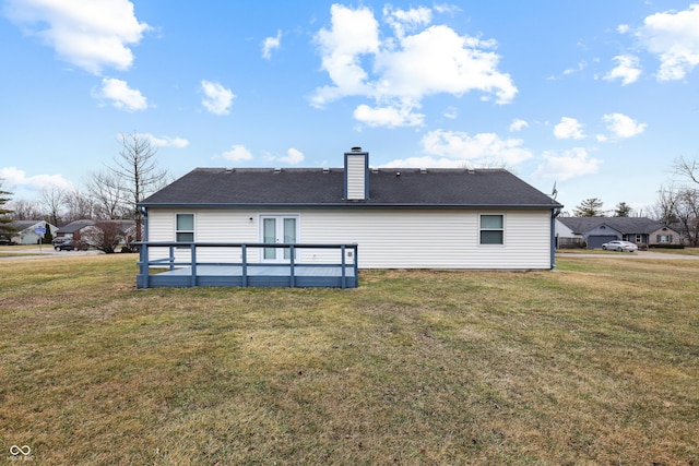 rear view of house featuring roof with shingles, a chimney, a lawn, and a wooden deck