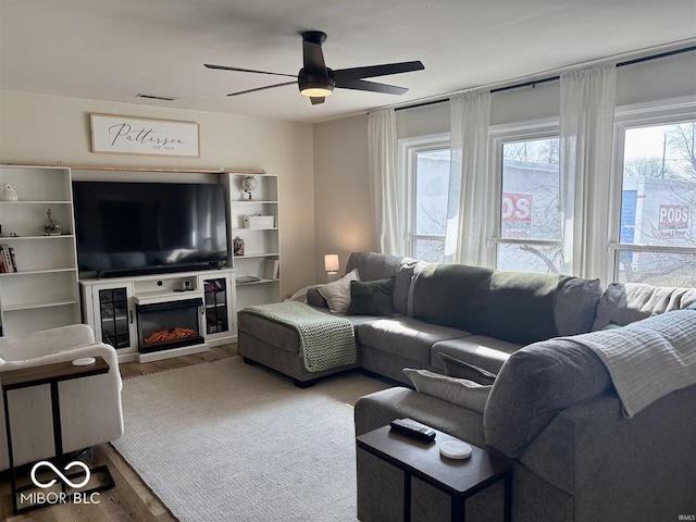 living area featuring a ceiling fan, wood finished floors, and a glass covered fireplace