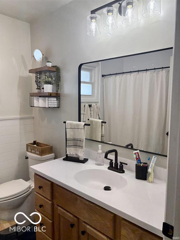 full bath featuring a wainscoted wall, toilet, tile walls, and vanity