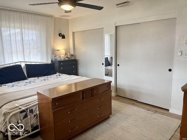 bedroom featuring two closets, ceiling fan, visible vents, and wood finished floors