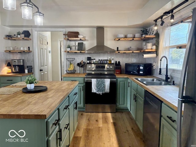 kitchen with butcher block countertops, green cabinets, wall chimney range hood, appliances with stainless steel finishes, and open shelves