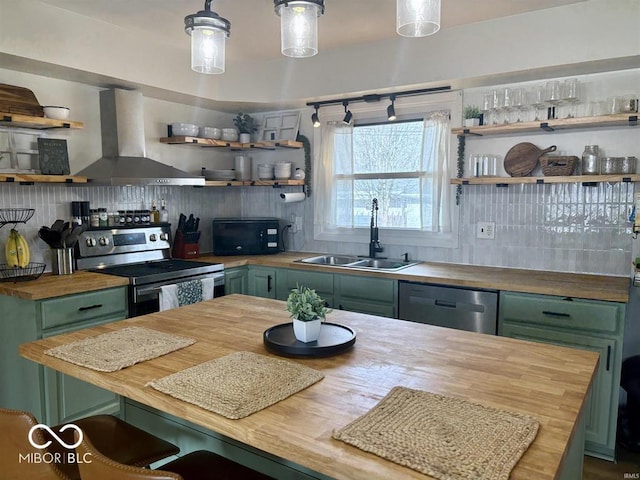 kitchen with wall chimney exhaust hood, butcher block counters, appliances with stainless steel finishes, green cabinets, and a sink