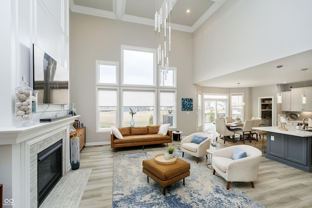 living area featuring light wood-type flooring, a high ceiling, ornamental molding, and a glass covered fireplace