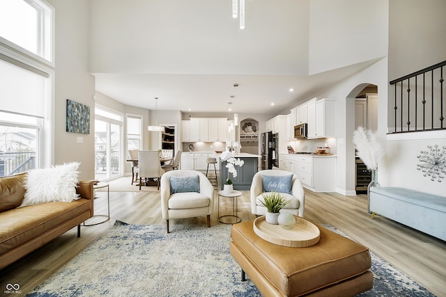 living area with arched walkways, a high ceiling, baseboards, stairway, and light wood finished floors