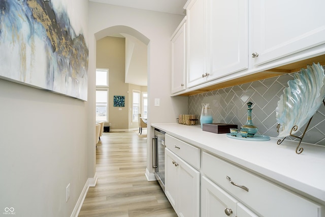 kitchen featuring light countertops, wine cooler, white cabinets, and decorative backsplash