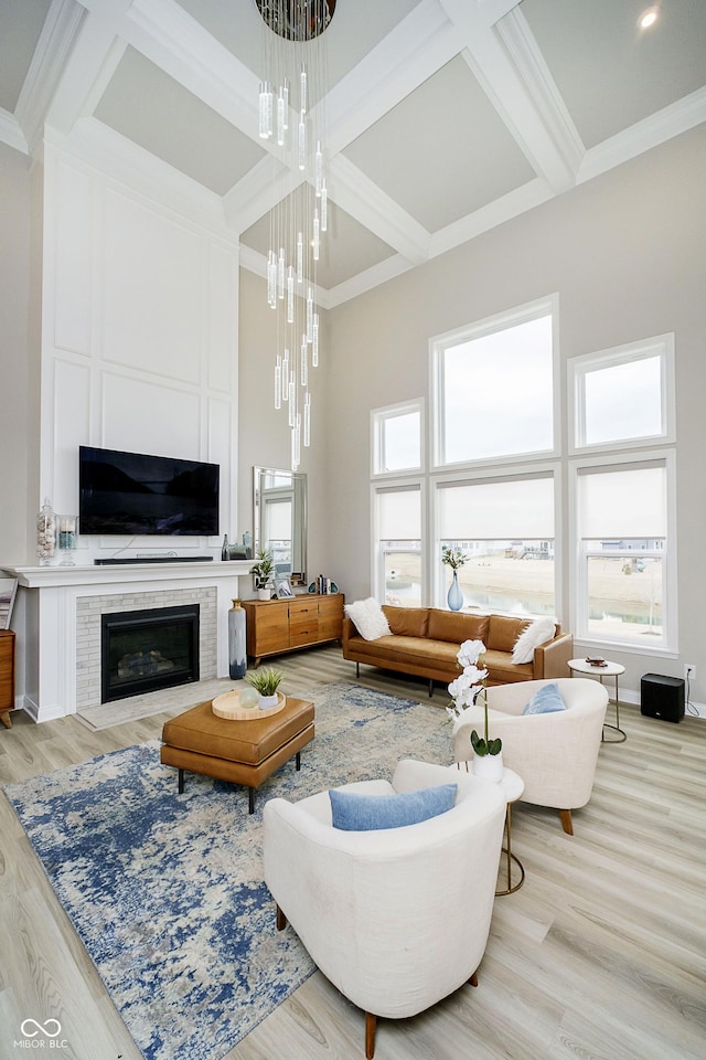 living room featuring coffered ceiling, wood finished floors, a high ceiling, crown molding, and a fireplace