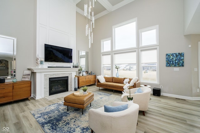 living area featuring light wood-style flooring, a brick fireplace, a towering ceiling, and baseboards