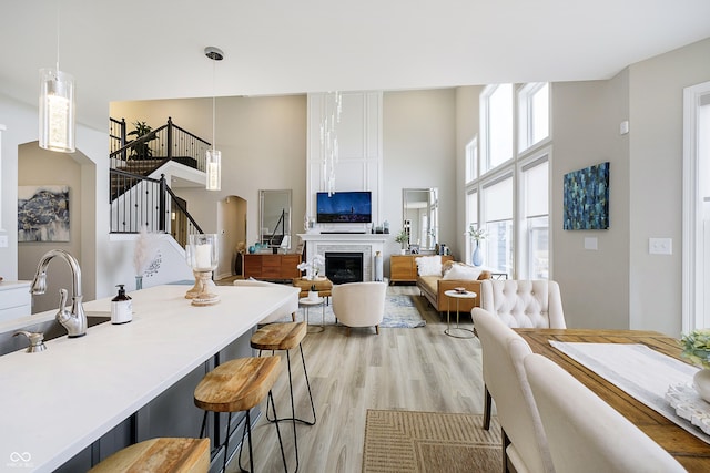 interior space featuring a breakfast bar area, a fireplace, a towering ceiling, white cabinetry, and light wood finished floors