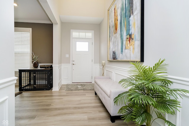 entrance foyer with ornamental molding, a decorative wall, wood finished floors, and wainscoting