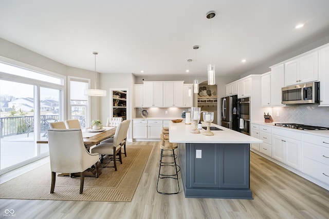 kitchen featuring tasteful backsplash, stainless steel appliances, light countertops, light wood-type flooring, and a sink