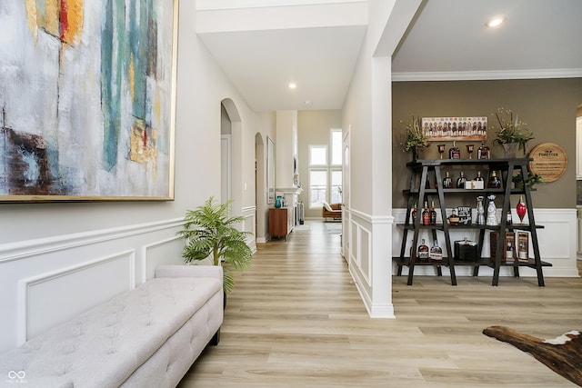 hall featuring light wood-style floors, wainscoting, and a decorative wall