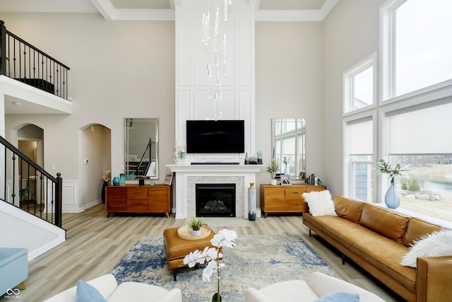 living room with arched walkways, a high ceiling, stairway, a brick fireplace, and light wood finished floors