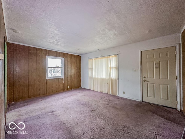 carpeted empty room with wooden walls and a textured ceiling