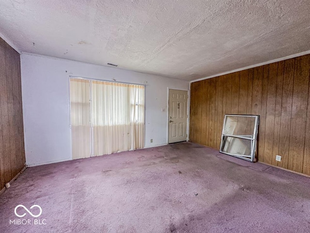 carpeted spare room featuring visible vents, wooden walls, and a textured ceiling