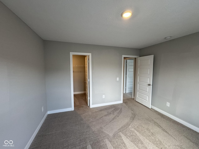 unfurnished bedroom featuring carpet, a spacious closet, baseboards, and a textured ceiling