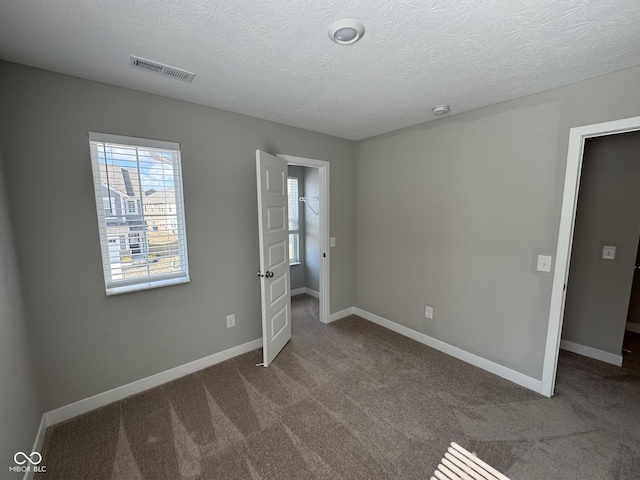 unfurnished bedroom featuring carpet, visible vents, a textured ceiling, and baseboards