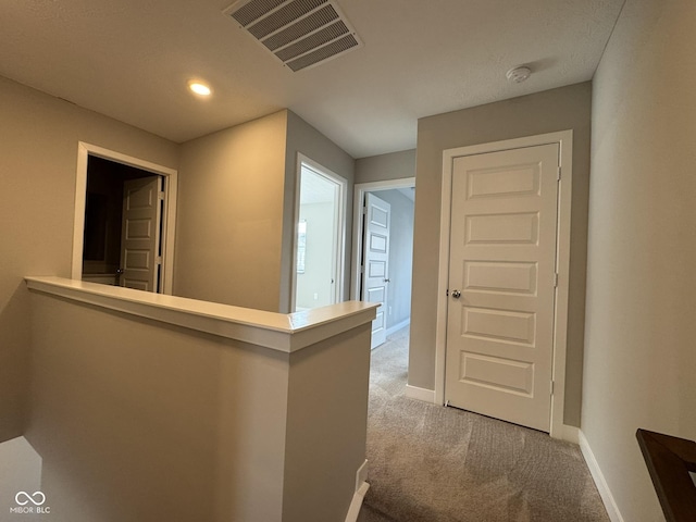 hall featuring carpet, baseboards, visible vents, and an upstairs landing