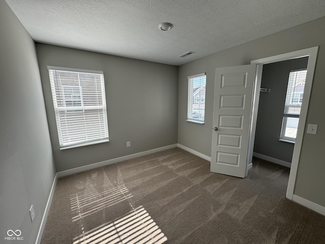 unfurnished bedroom with carpet, a textured ceiling, visible vents, and baseboards