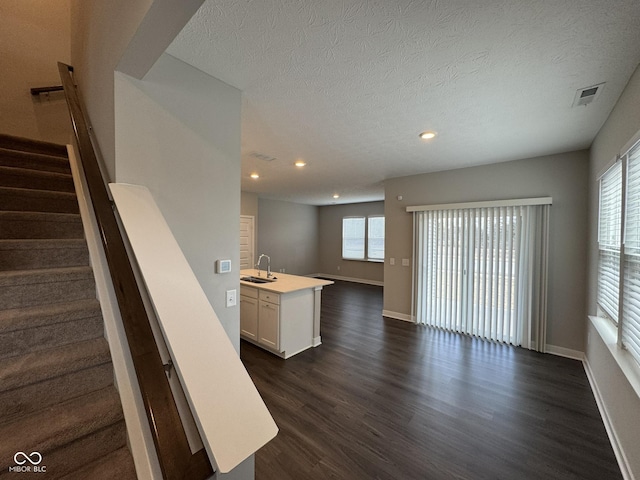 interior space featuring a sink, visible vents, open floor plan, light countertops, and dark wood finished floors