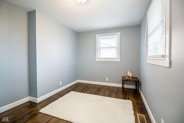 unfurnished room with dark wood-style floors, visible vents, and baseboards