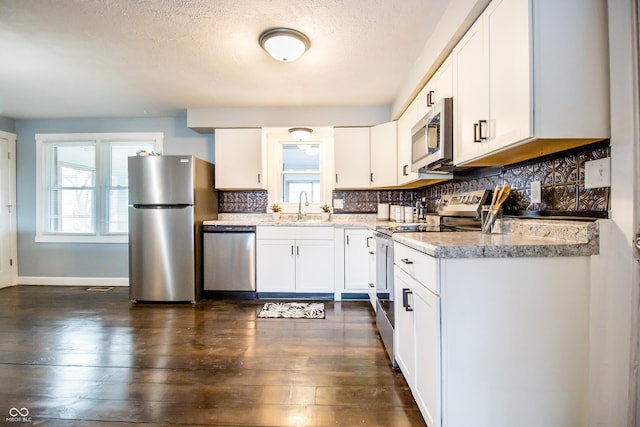 kitchen featuring white cabinets, dark wood finished floors, a sink, stainless steel appliances, and backsplash