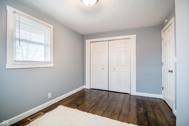 unfurnished bedroom featuring baseboards, visible vents, dark wood-style floors, a textured ceiling, and a closet