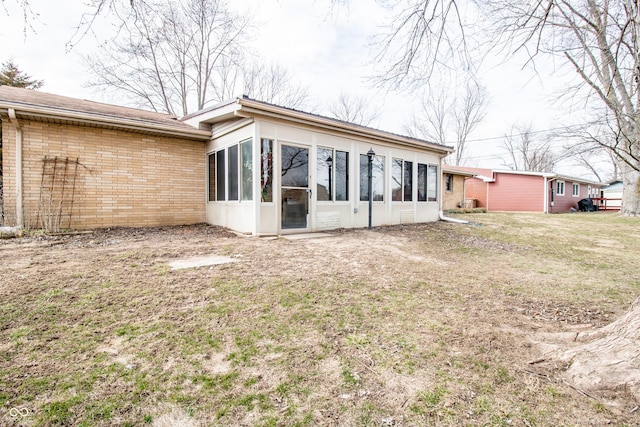 rear view of house with a sunroom, a yard, and brick siding