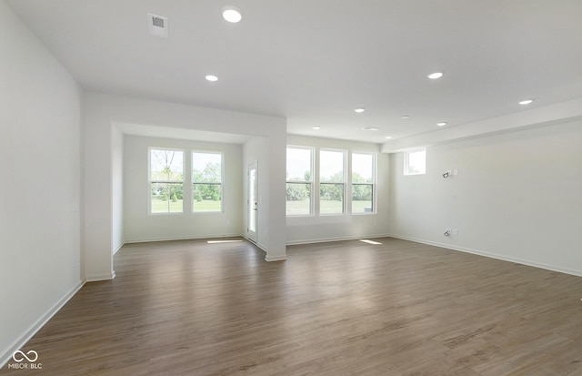 empty room featuring a wealth of natural light, visible vents, and wood finished floors