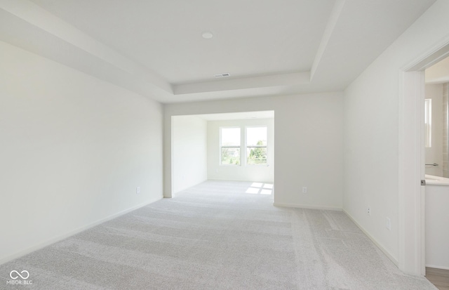 empty room featuring visible vents, a tray ceiling, baseboards, and light colored carpet