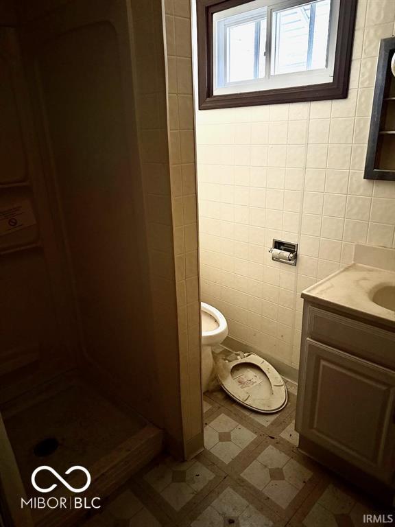 full bath featuring toilet, a stall shower, tile walls, and vanity