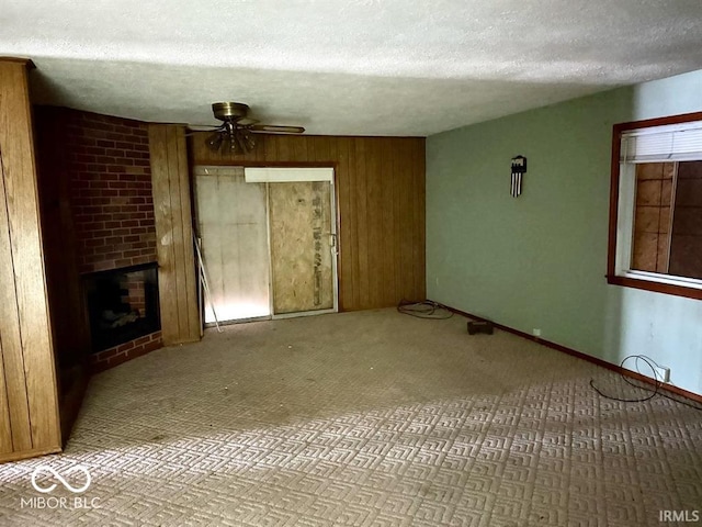 unfurnished living room featuring a fireplace, a ceiling fan, wood walls, a textured ceiling, and baseboards