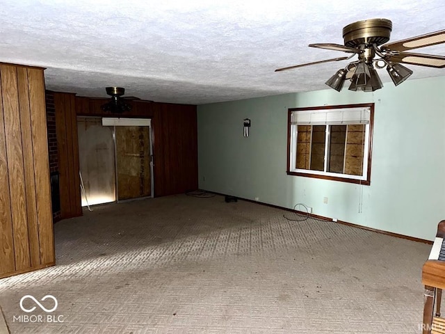 carpeted spare room with ceiling fan, a textured ceiling, baseboards, and wooden walls