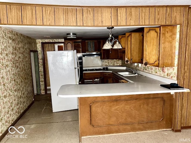 kitchen featuring brown cabinets, wallpapered walls, freestanding refrigerator, a sink, and extractor fan