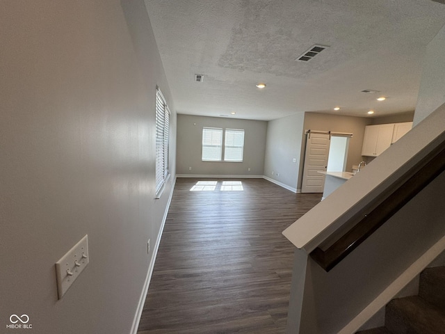 spare room with a textured ceiling, a barn door, baseboards, stairs, and dark wood-style floors