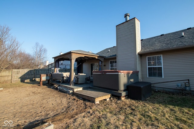 back of house with fence, a gazebo, roof with shingles, a chimney, and a hot tub