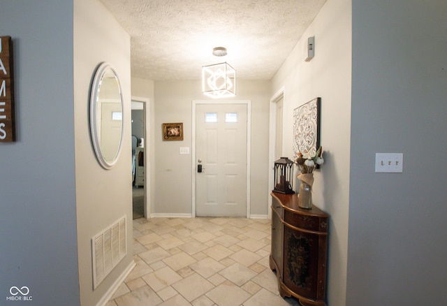 foyer entrance featuring stone finish floor, visible vents, a textured ceiling, and baseboards