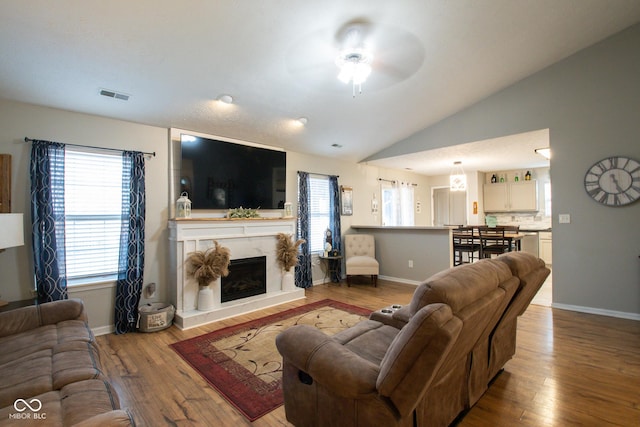 living area featuring visible vents, a high end fireplace, vaulted ceiling, wood finished floors, and baseboards