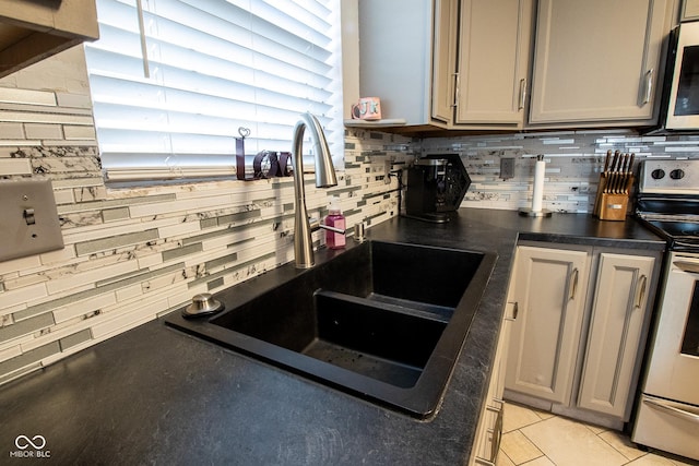 kitchen with decorative backsplash, dark countertops, gray cabinetry, stainless steel range with electric stovetop, and a sink