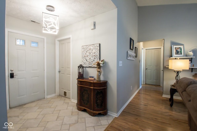 foyer featuring light wood finished floors, baseboards, and a textured ceiling