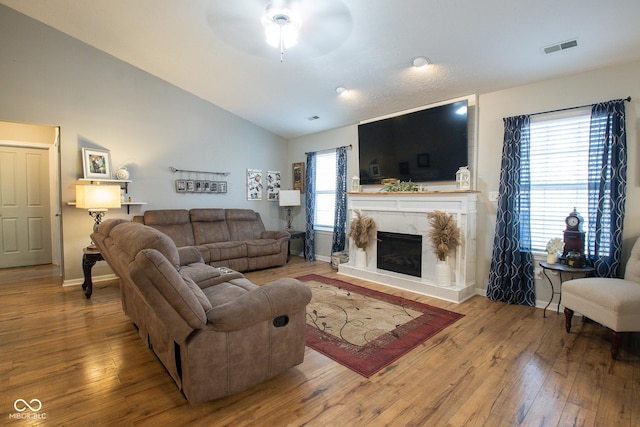 living area with visible vents, a premium fireplace, vaulted ceiling, baseboards, and hardwood / wood-style flooring