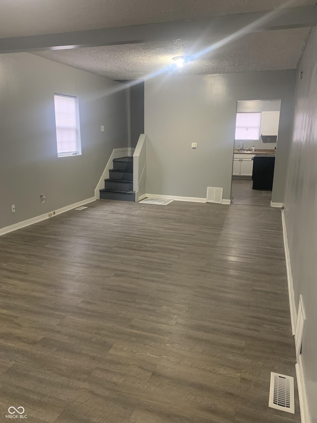 below grade area featuring a textured ceiling, stairway, dark wood finished floors, and visible vents