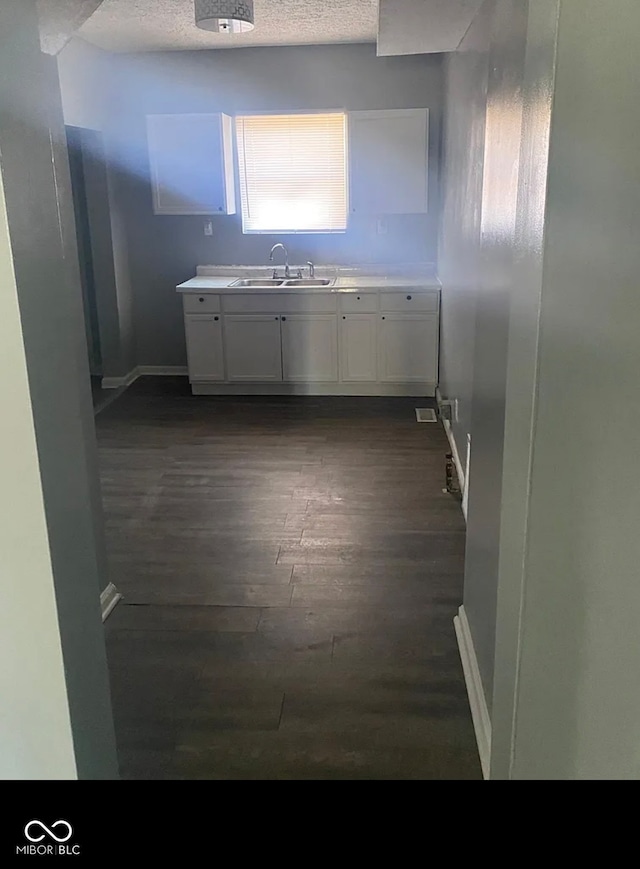 kitchen featuring dark wood finished floors, white cabinets, a sink, a textured ceiling, and baseboards