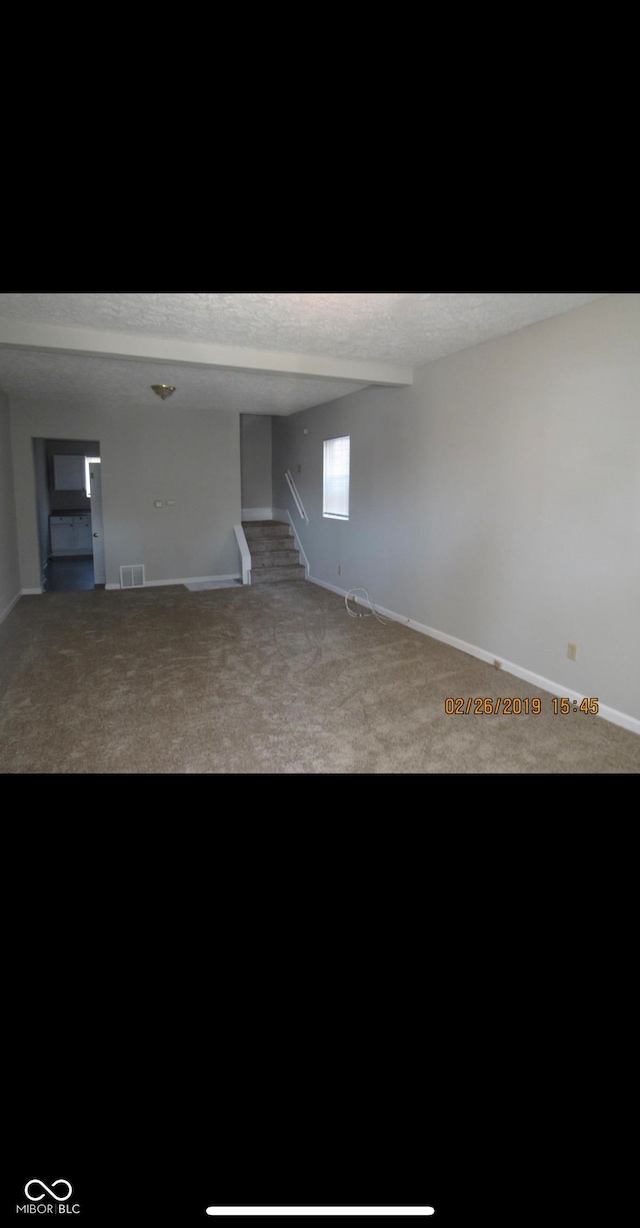 carpeted spare room with visible vents, stairway, and baseboards