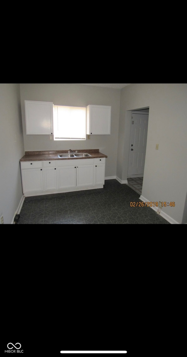 kitchen with baseboards, a sink, and white cabinets