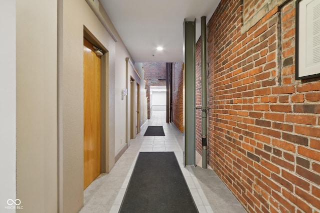 hallway featuring light tile patterned flooring and brick wall